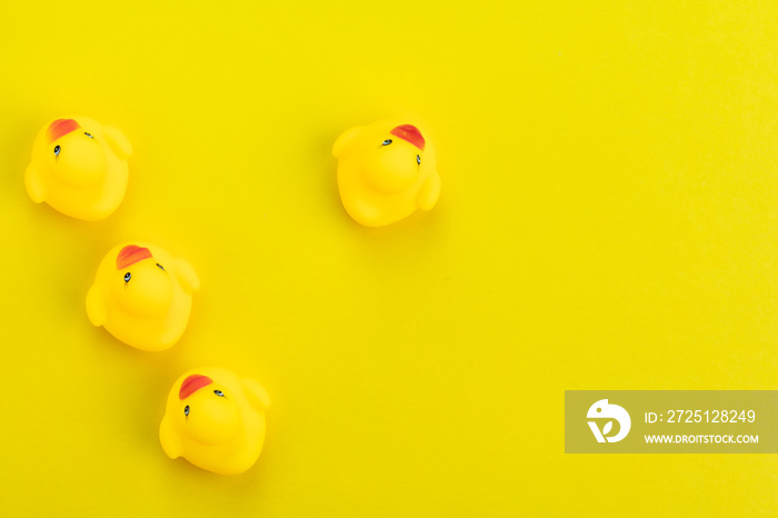 Row of yellow cute rubber ducks with one facing in a different direction on solid yellow background 