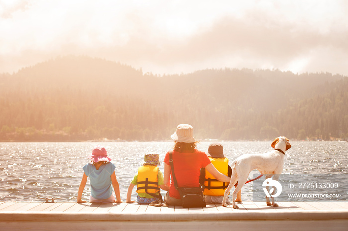 Family with three children (4-5, 6-7, 8-9) and dog sitting on jetty