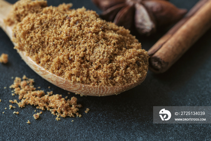 Natural brown sugar or unrefined sugar on wood spoon and cinnamon stick and anise on black granite t