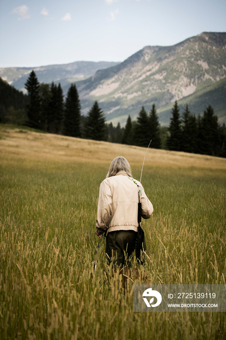 Rear view of senior man with fishing rod walking on grassy field