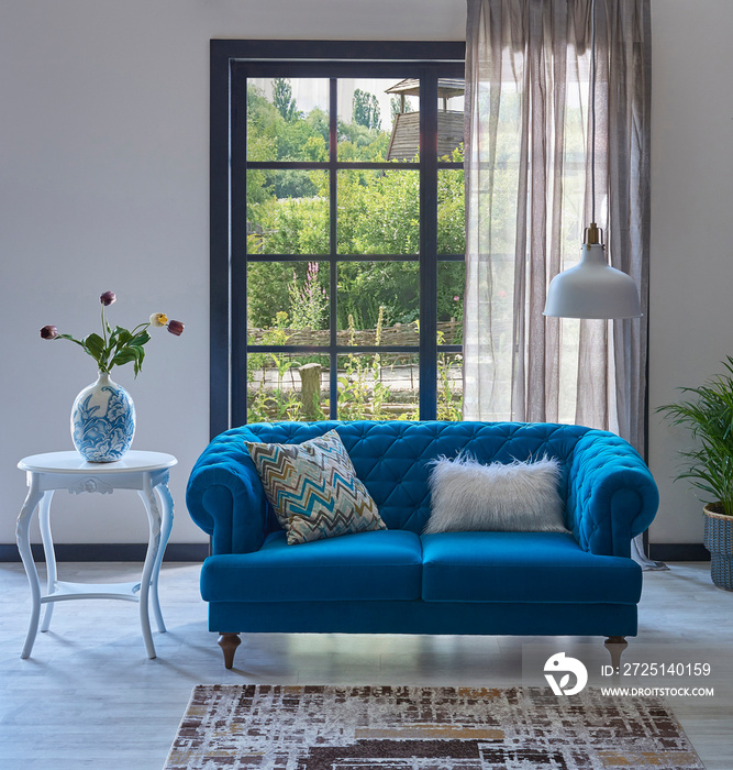 Blue classic sofa in front of the window, carpet design, white table vase of plant, lamp, garden bac