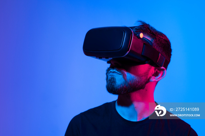 一名男子在黑暗的室内霓虹灯下玩视频游戏时使用VR耳机的肖像。