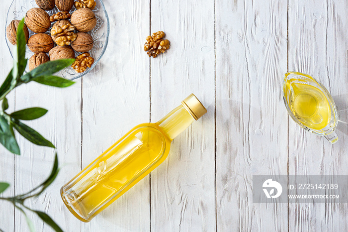 Walnut oil and a bunch of nuts on a white wooden table. Modern still life with oil bottle and glass 