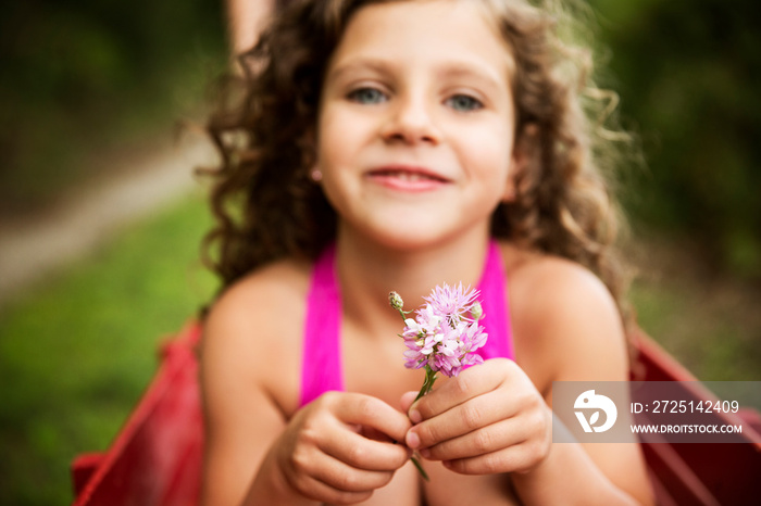 Girl (8-9) with curly hair holding pink flower