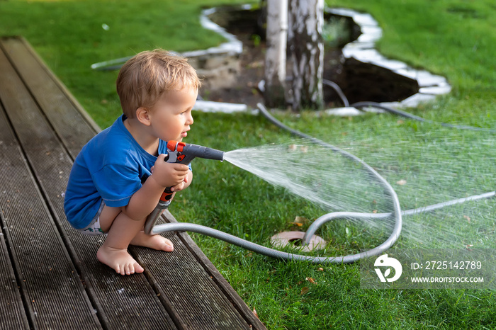 Cute adorable caucasian blond toddler boy enjoy having fun watering garden flower and lawn with hose