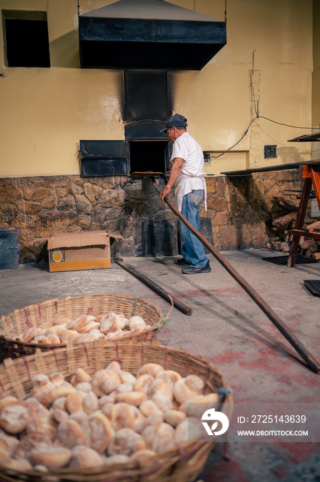 Panadero colocando el pan en un horno artesanal de leña. Panaderia Latina.