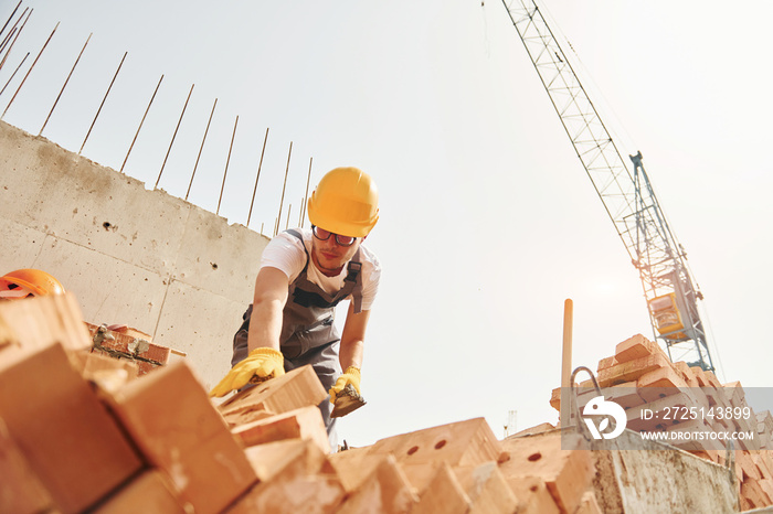 用砖。穿着制服的年轻建筑工人在未完工的建筑旁忙碌