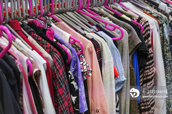 Various women clothing on mostly pink coat hangers inside charity second hand thrift shop