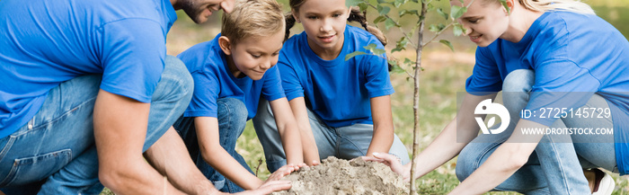 parents and two children planting young tree in forest, ecology concept, banner