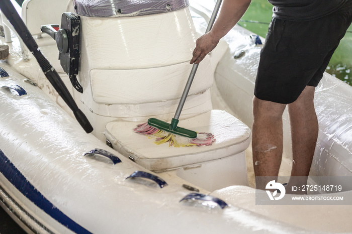 男子在车库用刷子和压力水系统清洗白色充气船。船舶服务和服务