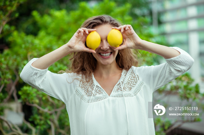 Woman in white holding two lemons and feeling cheerful