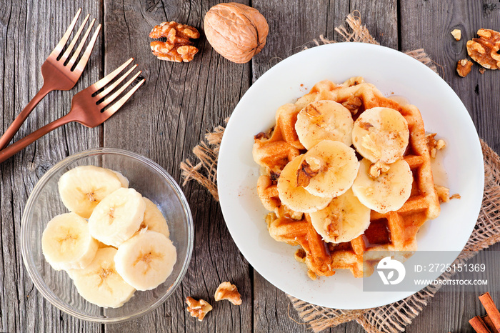 Breakfast waffle with bananas, walnuts and syrup. Above view table scene over a rustic wood backgrou