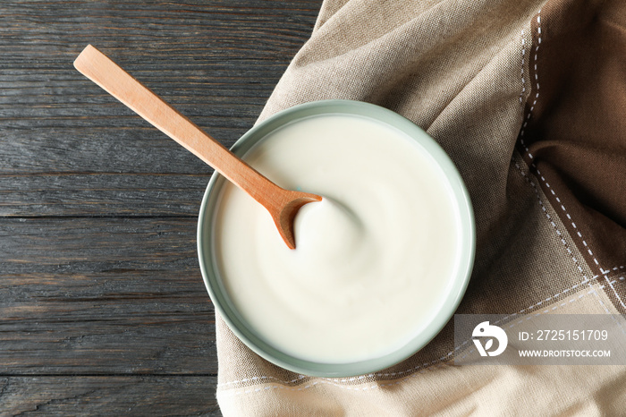 Bowl of sour cream yogurt, spoon and towel on wooden background