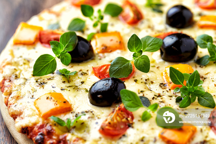 Pizza with cheese, orange pepper, cherry tomatoes, black olives and fresh oregano. Close up.