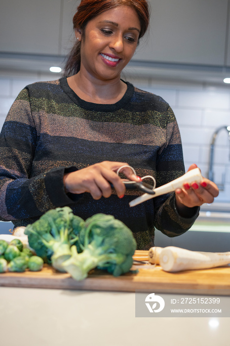 Smiling woman peeling parsley root in kitchen