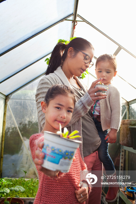 Girl holding plant pot with mother and sister in greenhouse