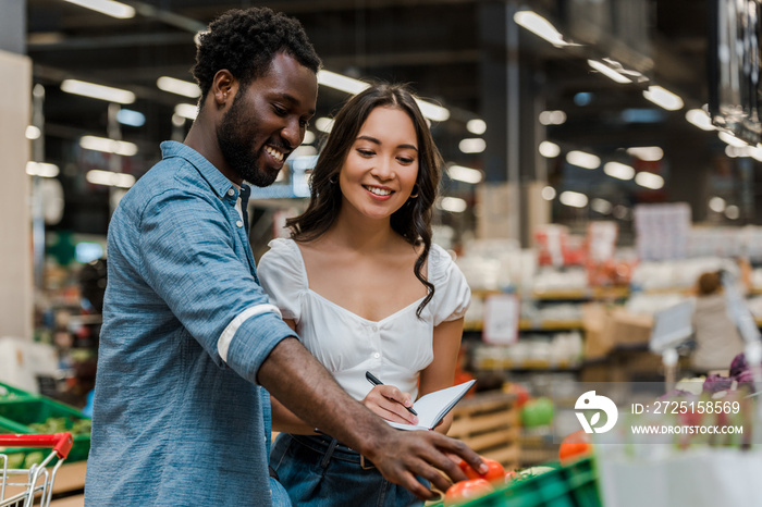 快乐的非裔美国男子在商店里靠近亚洲女子触摸红番茄的选择性焦点