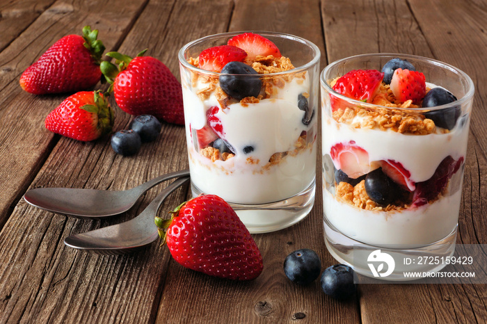 Strawberry and blueberry parfaits in glasses against a rustic dark wood background