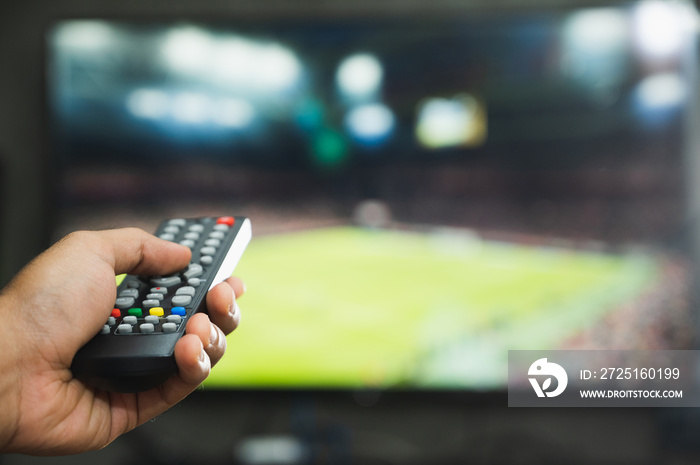 Young man holding television remote control watching football program. Hands pointing to tv screen s