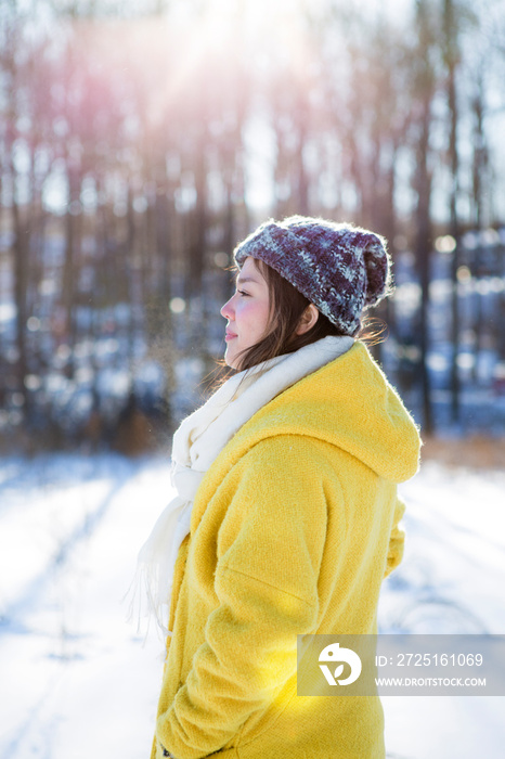 Side view of female in yellow coat and woolly hat at sunny winter day