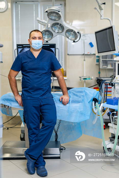 Young confident male doctor poses to the camera on modern surgery room background. Health care and l