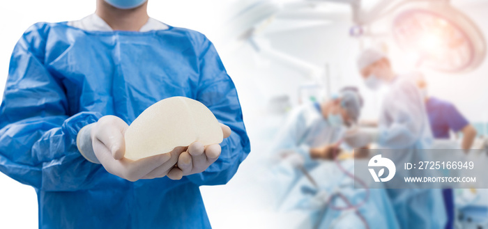 Surgeon in operation room is holding sterile breast silicone implant in hands.