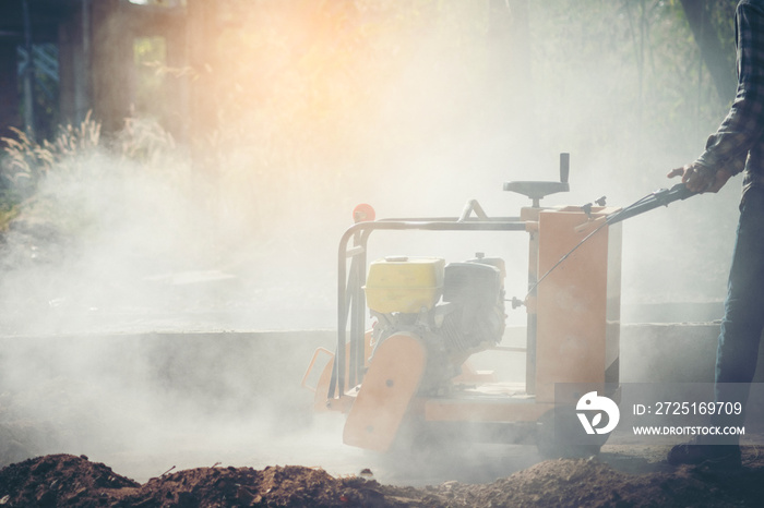 Construction worker using a concrete saw, cutting stones in a cloud of concrete dust for creating a 