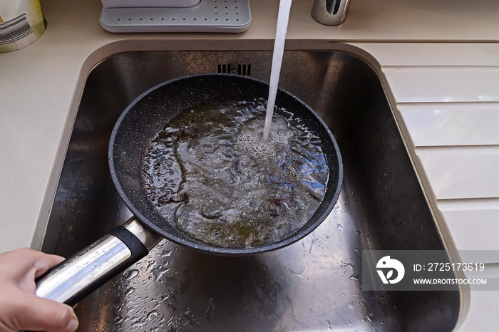 Frying pan with non-stick surface and hot oil under water tap flow in sink