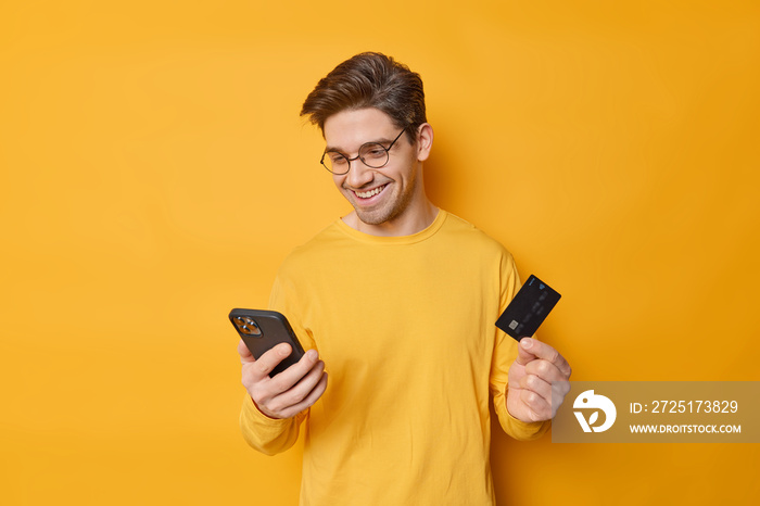 快乐的黑发男子使用手机和银行卡在网上订购som