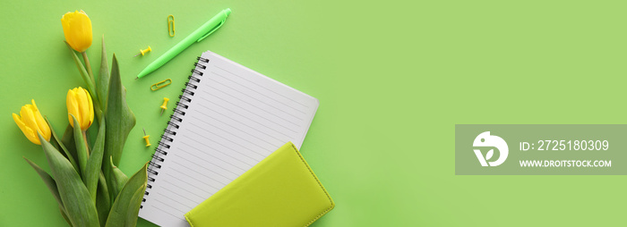 用笔记本、文具和黄色郁金香在绿色背景下创作，并留有文字空间