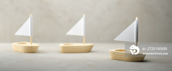 Conceptual image of three simple little wooden sailboats with sails over a grey background conceptua