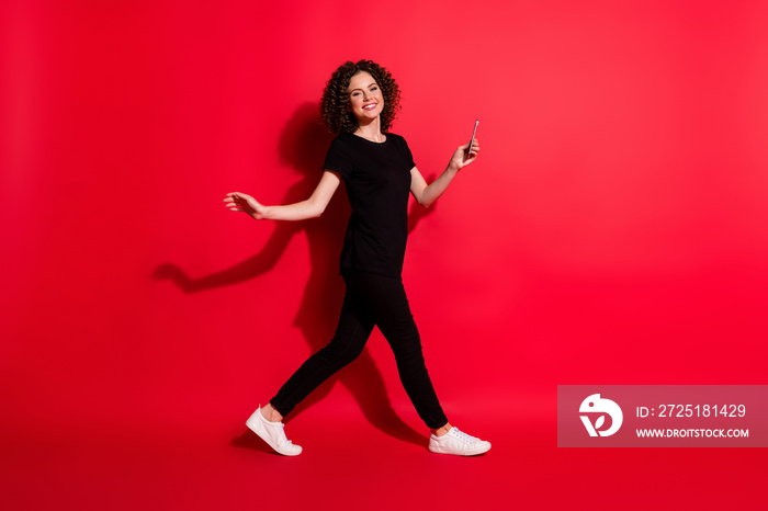 Full body photo of young happy attractive woman smile hold mobile go empty space isolated over red c
