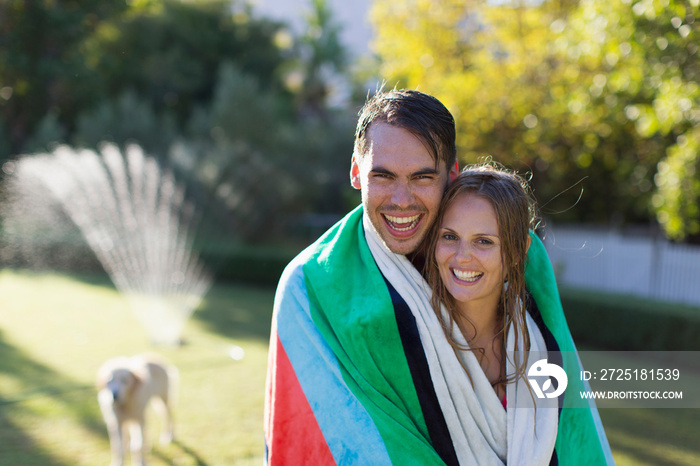 Portrait happy couple wrapped in towel in sunny backyard