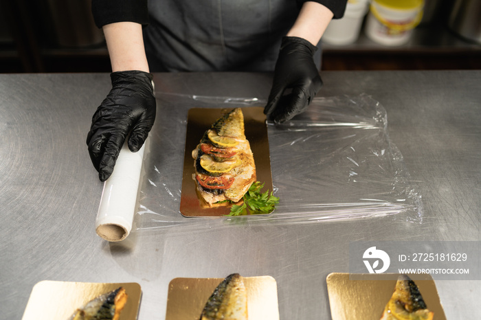 Woman using cling film to store food on the table in a restaurant in the kitchen. A roll of transpar