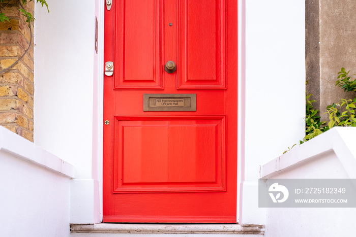 Beautiful red door with letterbox in a white house facade in Notting Hill