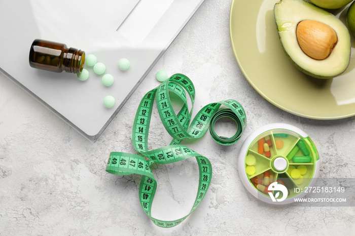 Weight loss pills, scales, fruits and measuring tape on light background