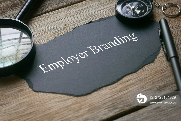 Magnifying glass,pen,compass and piece of black paper written with Employer Branding on wooden backg