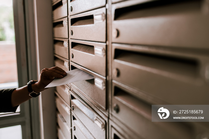 Female hand dropping envelope into mailbox in apartment building.