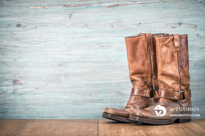 Wild West old retro leather cowboy boots front textured wooden wall background. Vintage style filter