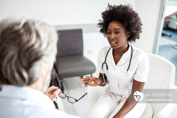 African American doctor consoling her mature patient in waiting room at medical clinic.