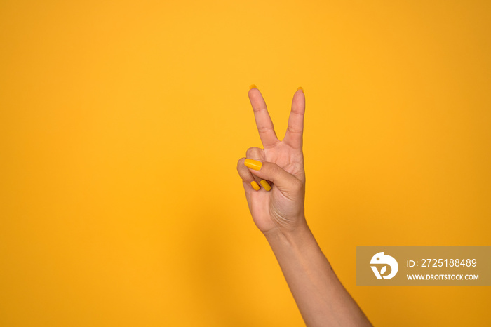 V sign. Female hand shows two fingers or peace gesture. Cut out on yellow background. Copy space.