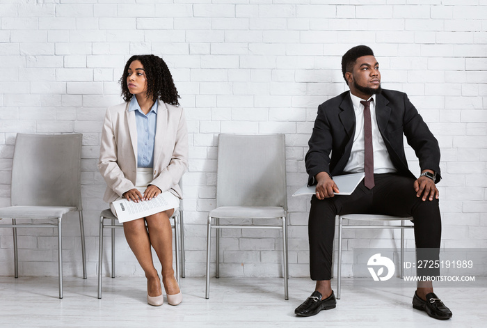 Black man and woman looking in opposite directions, feeling competitive while waiting for job interv