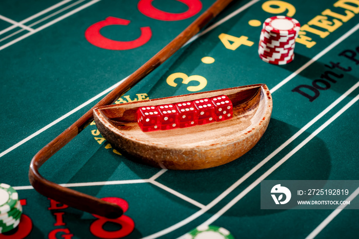 Full set of 5 dice in a wooden bowl next to the stick on a craps table with stacks of casino chip ar