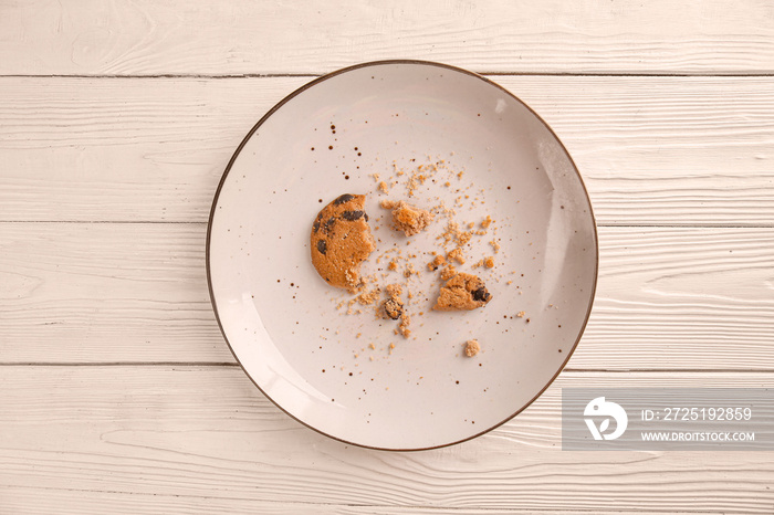 Plate with crushed cookie on light wooden background