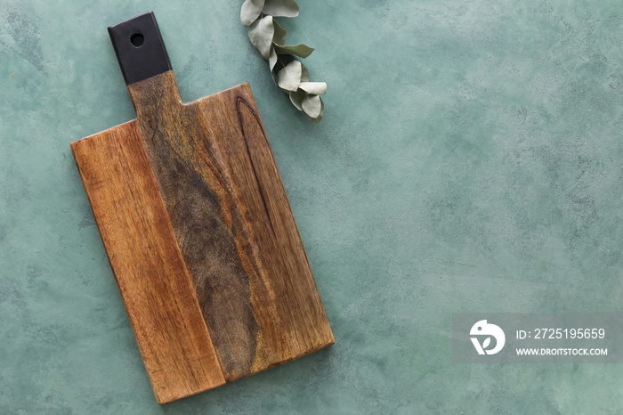 Wooden cutting board and eucalyptus branch on green background