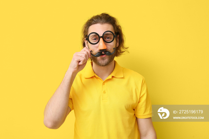 Funny young man in disguise on yellow background. April fools day celebration