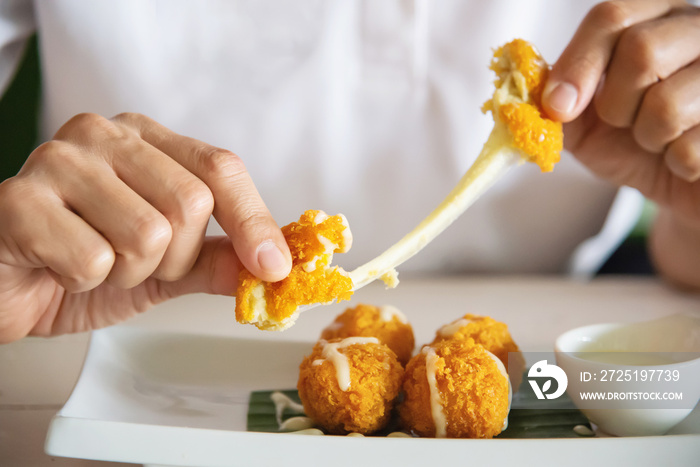 Man is going to eat sticky stretch fried cheese ball. Photo is focused at cheese ball