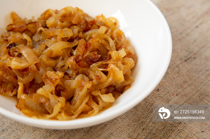 Homemade caramelized onions on a white plate, side view. Close-up.