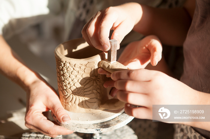 Unrecognizable child putting stamps onto clay cup at pottery workshop
