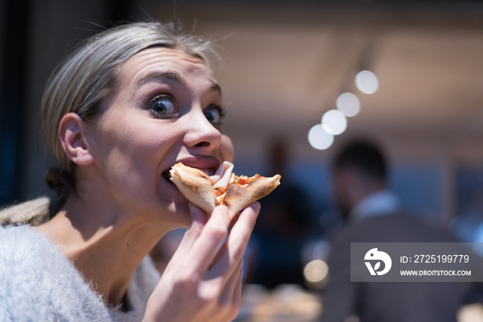 Beautiful woman eating pizza and drinking cola while sitting inside expres restaurant late at night.